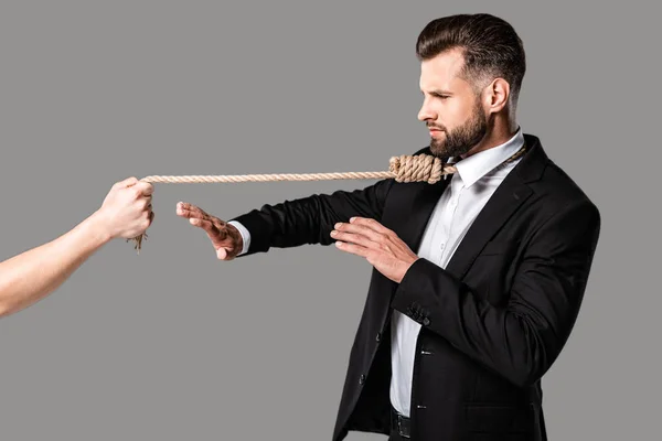 Businessman in black suit with noose on neck showing stop gesture to murderer with rope isolated on grey — Stock Photo