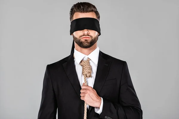Hombre de negocios con los ojos vendados en traje negro con soga en el cuello aislado en gris - foto de stock
