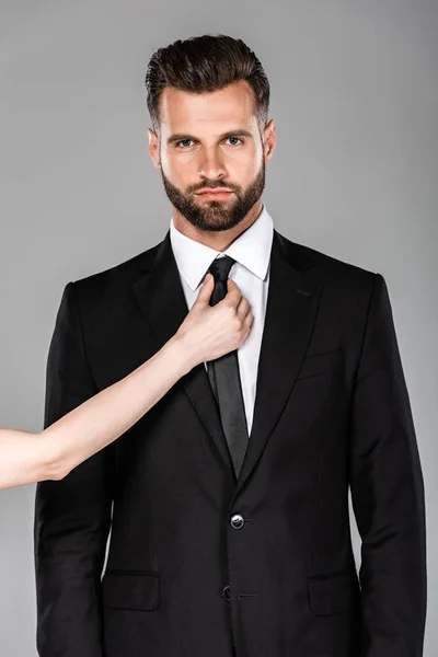 Жінка зав'язує краватку на красивого бізнесмена в чорному костюмі ізольовано на сірому — стокове фото
