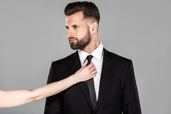 Mujer tocando corbata en hombre de negocios en traje negro aislado en gris - foto de stock
