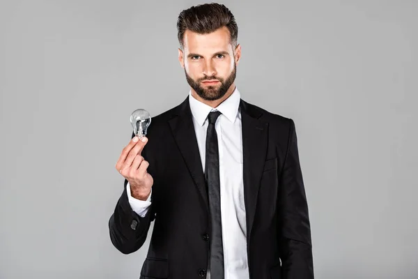 Handsome successful businessman in black suit holding light bulb isolated on grey — Stock Photo