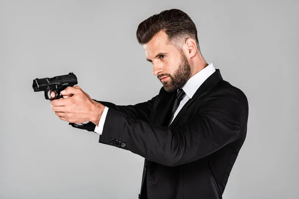 Schöner Agent im schwarzen Anzug zielte mit Waffe isoliert auf grau — Stockfoto