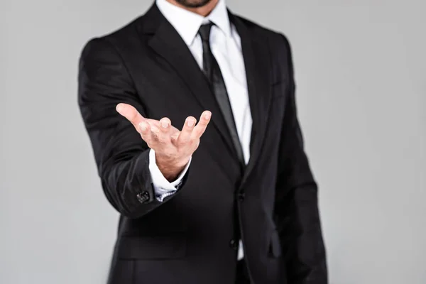 Vista parcial de hombre de negocios en traje negro con la mano mendicidad aislado en gris - foto de stock