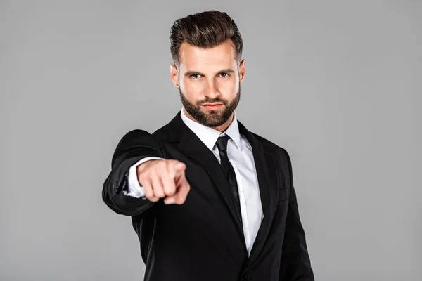 Exitoso hombre de negocios en traje negro apuntando con el dedo a la cámara aislado en gris - foto de stock