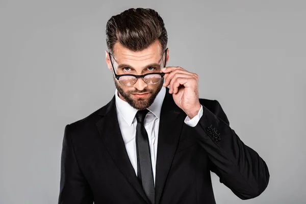 Confiant homme d'affaires réussi en costume noir et lunettes isolé sur gris — Photo de stock