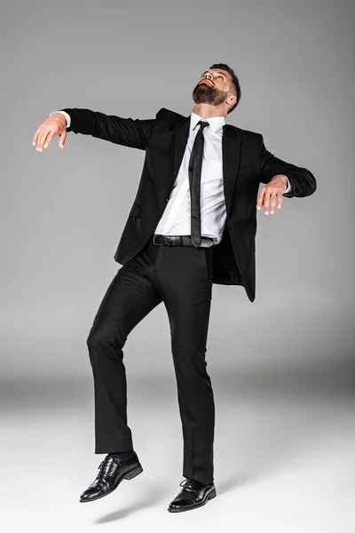 Vista completa del hombre de negocios zombi en traje negro caminando sobre gris - foto de stock