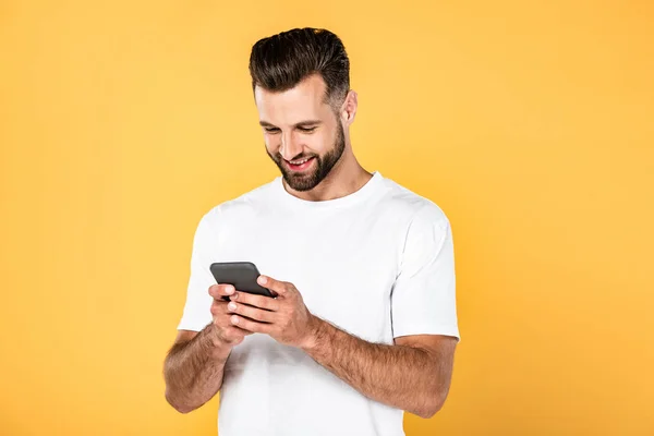 Smiling handsome man in white t-shirt using smartphone isolated on yellow — Stock Photo