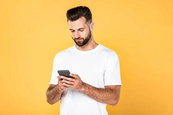 Hombre guapo en camiseta blanca usando teléfono inteligente aislado en amarillo - foto de stock
