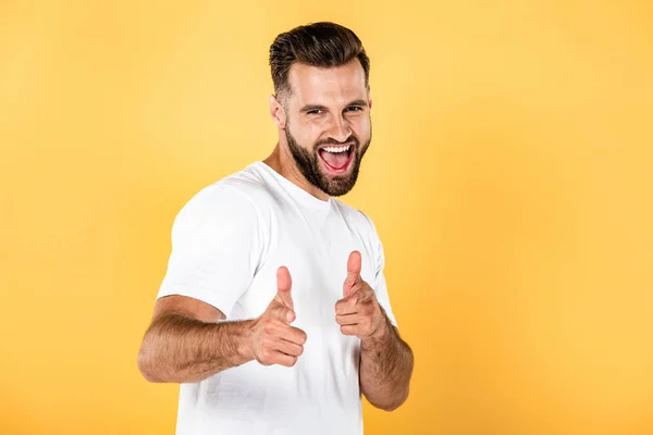 Hombre guapo feliz en camiseta blanca apuntando con los dedos a la cámara aislada en amarillo - foto de stock