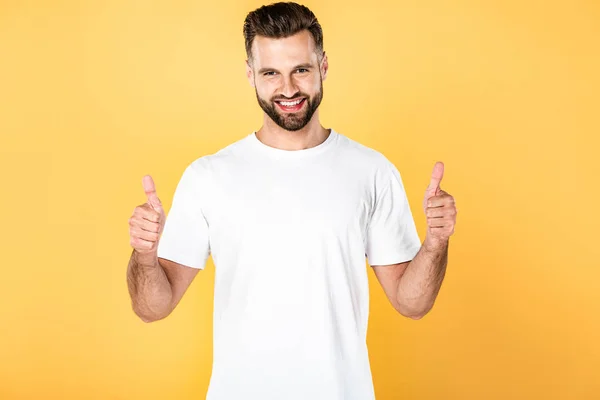 Hombre guapo feliz en camiseta blanca mostrando los pulgares hacia arriba aislado en amarillo - foto de stock