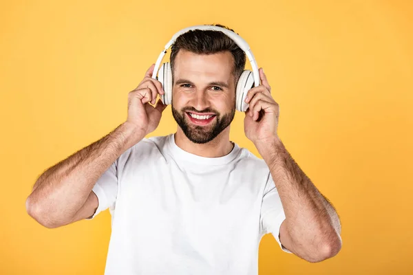 Felice uomo in t-shirt bianca ascoltando musica in cuffia isolata su giallo — Foto stock