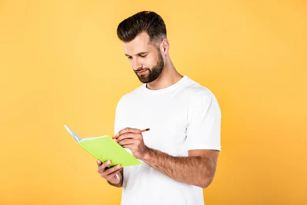 Hombre guapo en camiseta blanca escrito en cuaderno aislado en amarillo - foto de stock