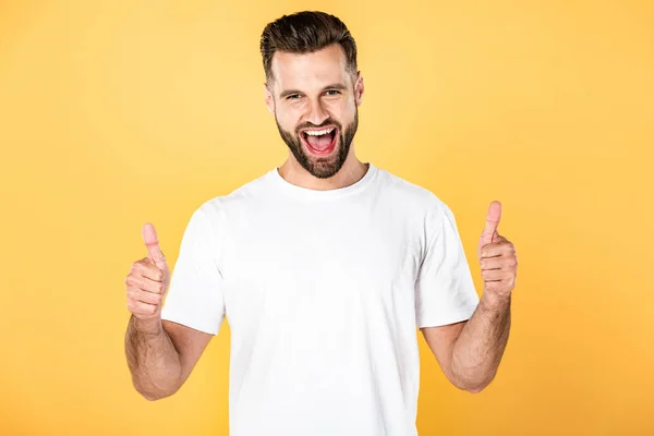 Excitado hombre guapo en camiseta blanca mostrando pulgares hacia arriba aislado en amarillo - foto de stock