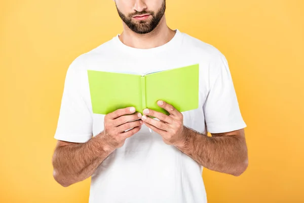 Vue recadrée de l'homme barbu en t-shirt blanc livre de lecture isolé sur jaune — Photo de stock