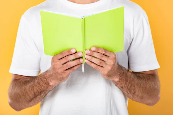 Partial view of man in white t-shirt reading book isolated on yellow — Stock Photo