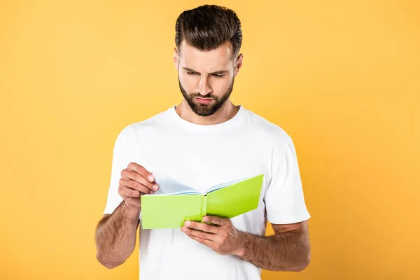 Handsome man in white t-shirt reading book isolated on yellow — Stock Photo