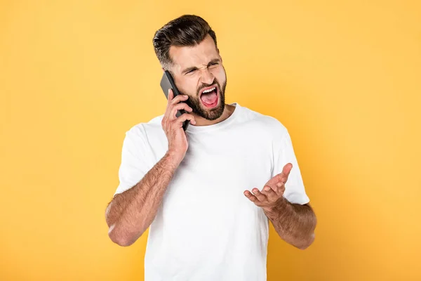 Wütender gutaussehender Mann in weißem T-Shirt, der auf dem Smartphone redet und isoliert auf gelb schreit — Stockfoto