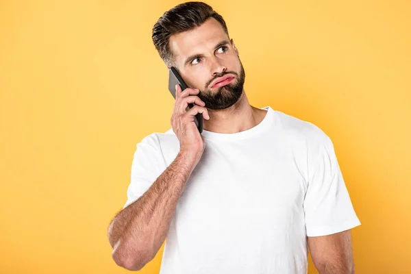 Homme frustré en t-shirt blanc parlant sur smartphone isolé sur jaune — Photo de stock
