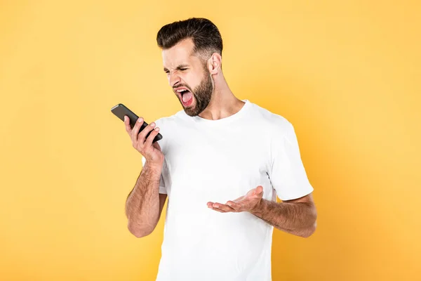 Homem zangado em t-shirt branca gritando em smartphone isolado em amarelo — Fotografia de Stock