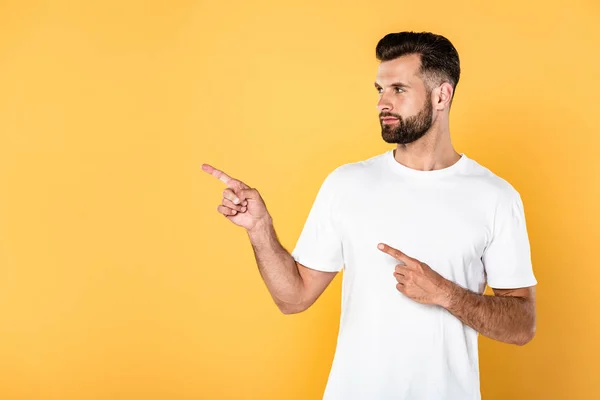 Hombre guapo en camiseta blanca señalando con los dedos a un lado aislado en amarillo - foto de stock