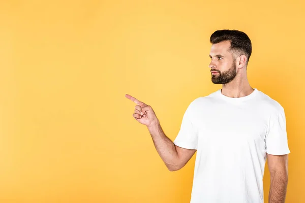 Schöner Mann im weißen T-Shirt zeigt mit dem Finger zur Seite isoliert auf gelb — Stockfoto