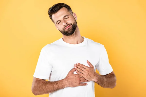 Heureux bel homme en t-shirt blanc touchant coeur isolé sur jaune — Photo de stock