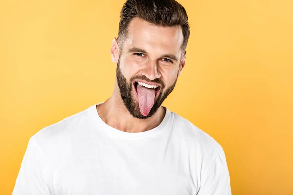 Handsome funny man in white t-shirt showing tongue isolated on yellow — Stock Photo
