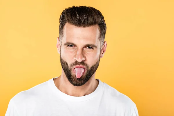 Funny man in white t-shirt showing tongue isolated on yellow — Stock Photo