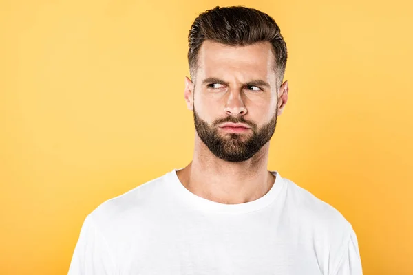 Hombre guapo preocupado en camiseta blanca mirando hacia otro lado aislado en amarillo - foto de stock