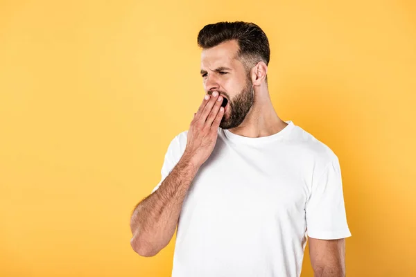 Sleepy handsome man in white t-shirt yawning isolated on yellow — Stock Photo