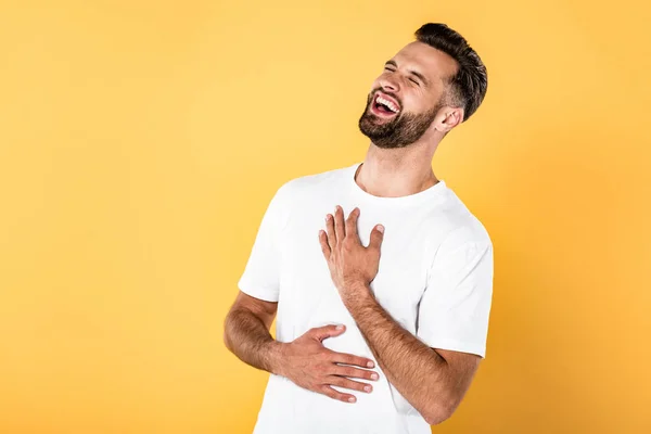 Homem bonito feliz na t-shirt branca rindo isolado no amarelo — Fotografia de Stock