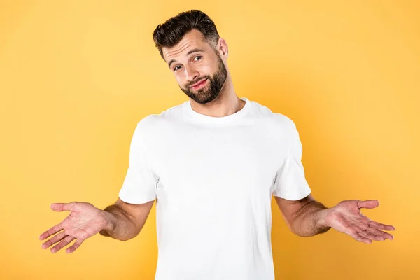 Smiling handsome man in white t-shirt showing shrug gesture isolated on yellow — Stock Photo
