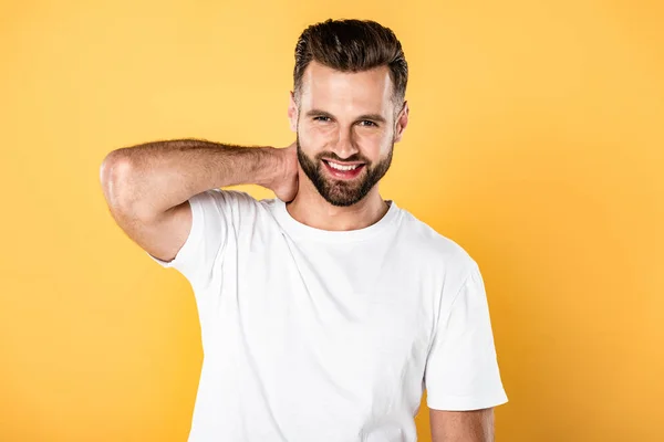 Happy handsome man in white t-shirt touching neck isolated on yellow — Stock Photo