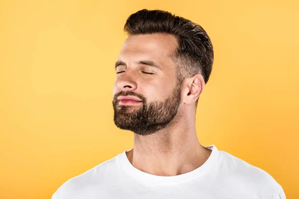 Homem bonito alegre na t-shirt branca com os olhos fechados isolados no amarelo — Fotografia de Stock