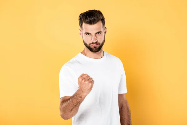 Homme beau en colère en t-shirt blanc montrant poing isolé sur jaune — Photo de stock