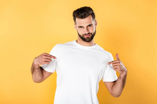 Egotistical handsome man in white t-shirt pointing with fingers at himself isolated on yellow — Stock Photo