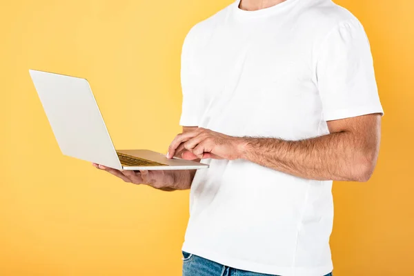 Vista recortada del hombre en camiseta blanca usando el ordenador portátil aislado en amarillo - foto de stock