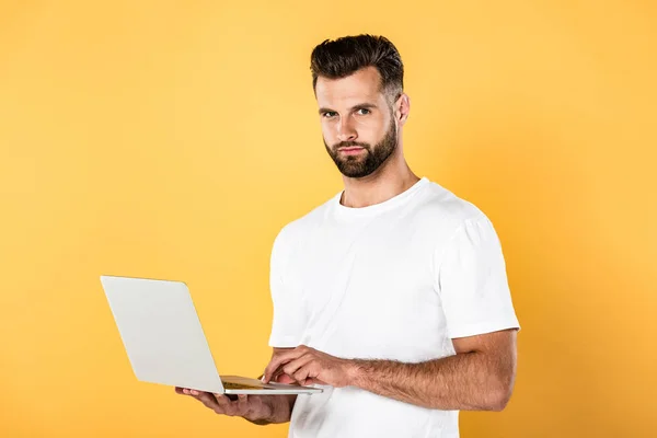 Hombre guapo en camiseta blanca usando portátil aislado en amarillo - foto de stock
