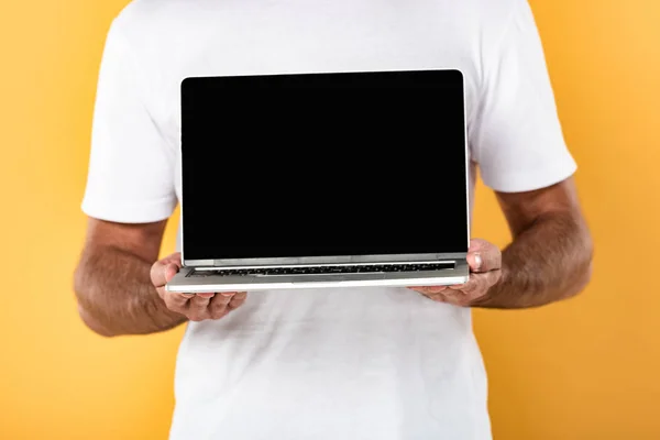 Vue recadrée de l'homme en t-shirt blanc montrant ordinateur portable avec écran blanc isolé sur jaune — Photo de stock