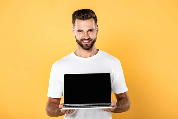 Felice bell'uomo in t-shirt bianca mostrando laptop con schermo bianco isolato su giallo — Foto stock