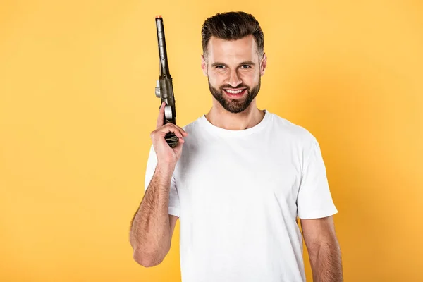 Smiling handsome man in white t-shirt holding revolver isolated on yellow — Stock Photo