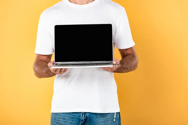 Vista parcial del hombre en camiseta blanca que muestra el ordenador portátil con pantalla en blanco aislado en amarillo - foto de stock