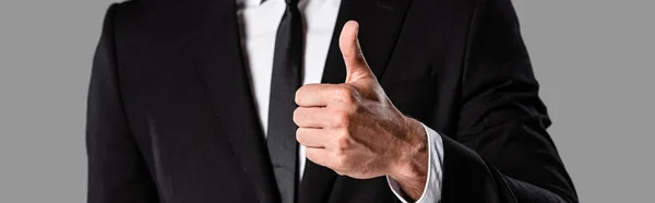 Vista recortada de hombre de negocios en traje negro que muestra el pulgar hacia arriba aislado en gris, tiro panorámico - foto de stock