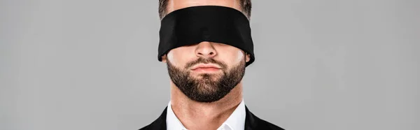 Prise de vue panoramique d'un élégant homme d'affaires aux yeux bandés en costume noir isolé sur gris — Photo de stock