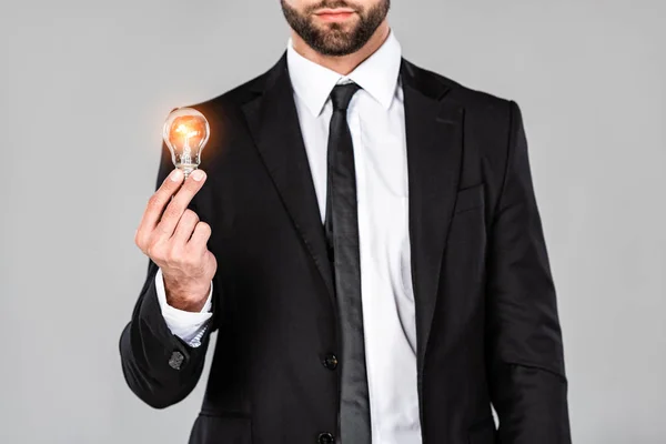 Cropped view of businessman in black suit holding glowing light bulb isolated on grey — Stock Photo