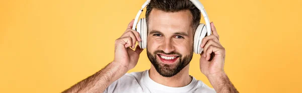 Plano panorámico del hombre feliz en camiseta blanca escuchando música en auriculares aislados en amarillo - foto de stock