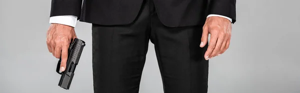Vista parcial del agente en traje negro con pistola aislada en gris, tiro panorámico - foto de stock