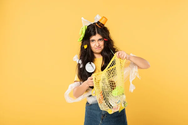 Mujer joven molesta con la basura en el pelo bolsa de retención con basura aislada en amarillo - foto de stock