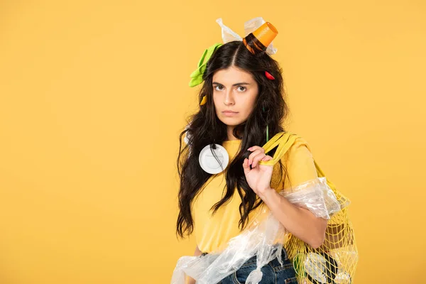 Sad woman with trash in hair holding bag with rubbish isolated on yellow — Stock Photo