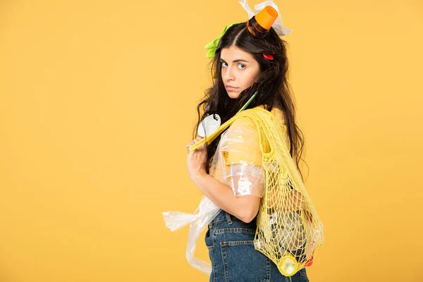 Chica confundida con la basura en la bolsa de sujeción del cabello con basura aislada en amarillo - foto de stock